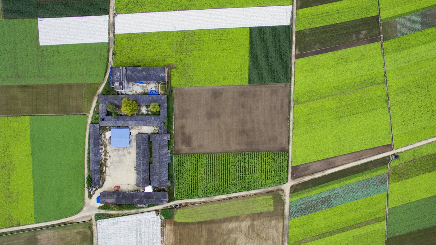 Aerial view of farmstead surrounded by green fields and tilled earth.