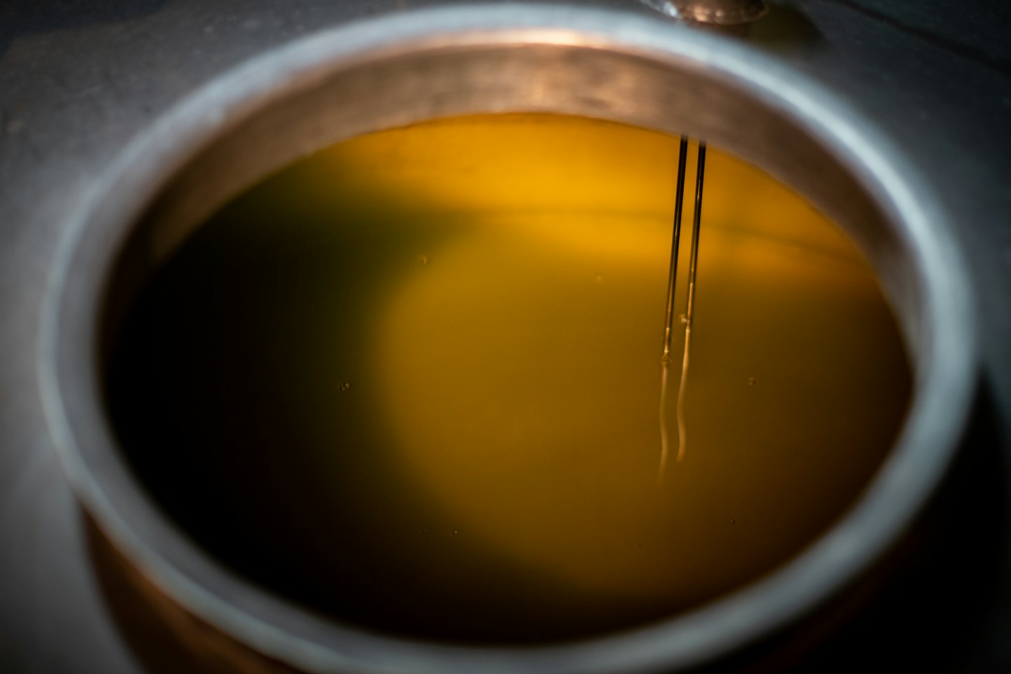 Two metal rods submerge into golden liquid inside an industrial vat.