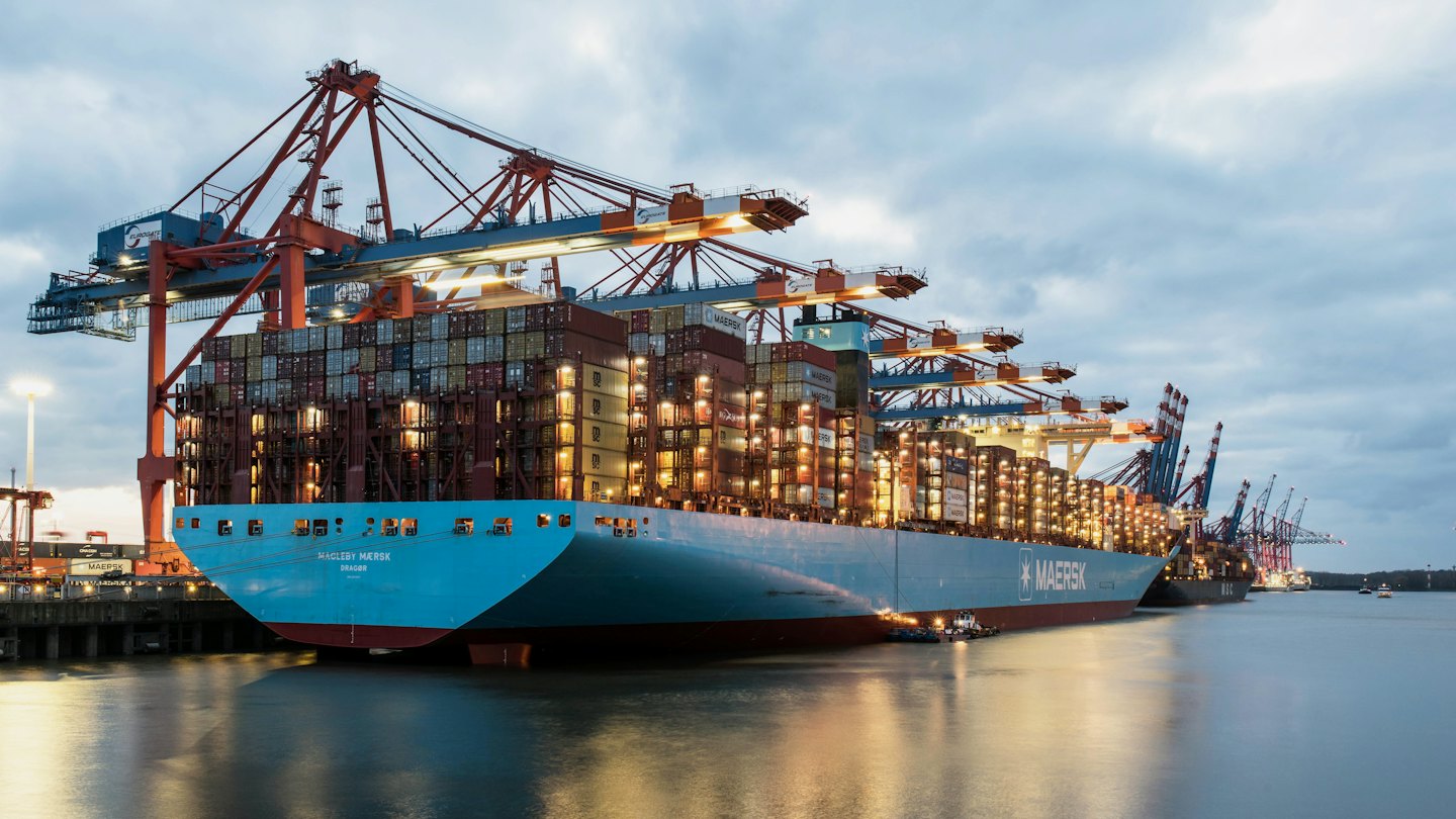 Blue container ship docked at a busy port at twilight.